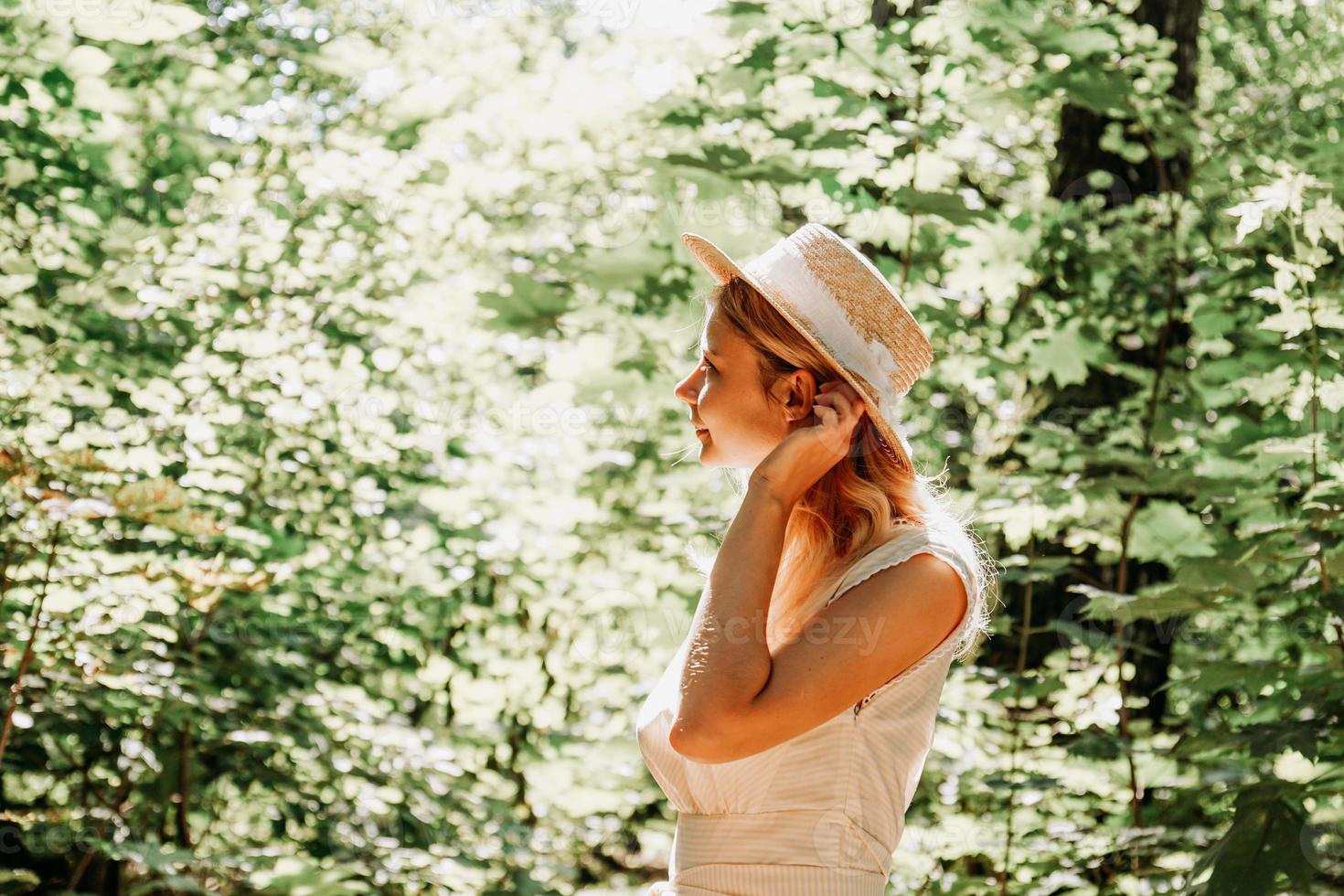 schöne junge Frau mit Strohhut und weißem Kleid in einem grünen Park foto