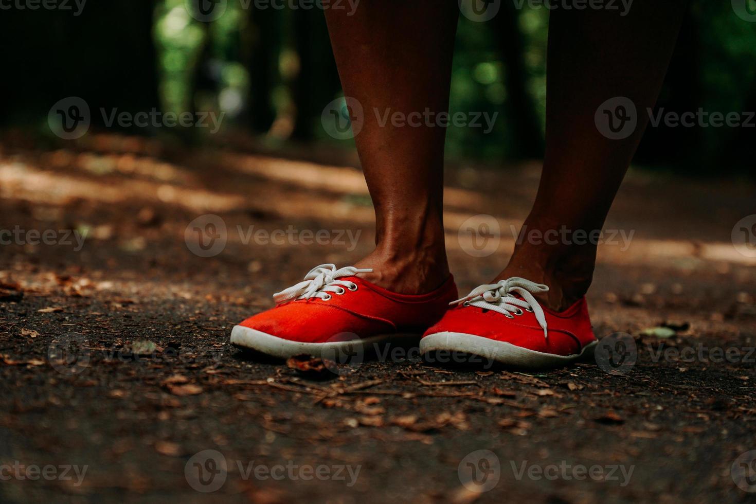 Beine in roten Turnschuhen auf einem Herbstweg im Park. schwarze Lederbeine foto
