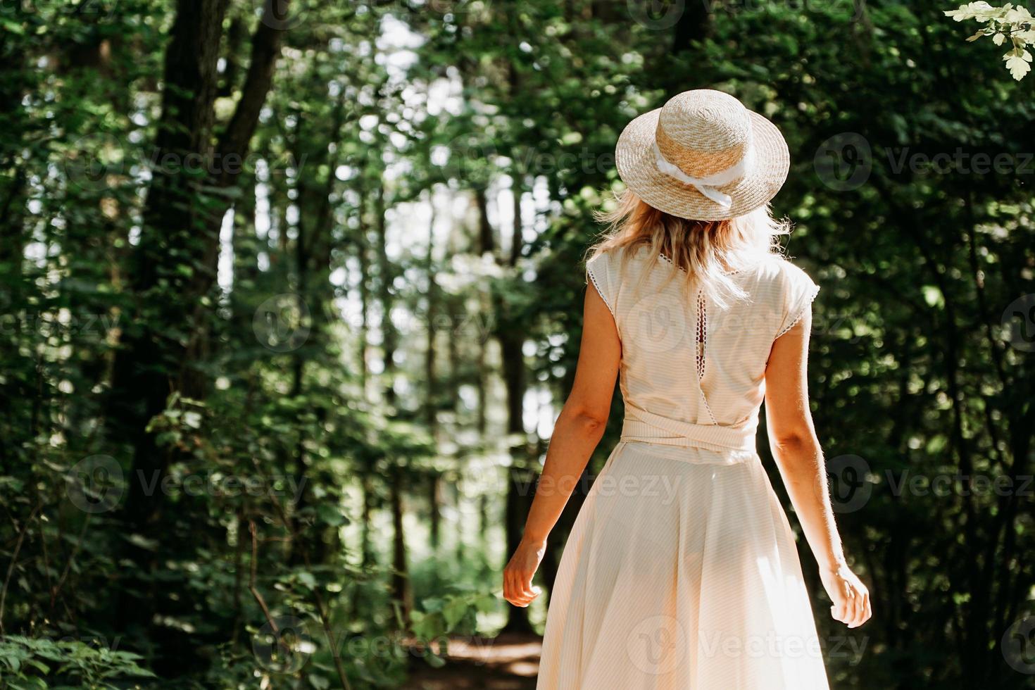 schöne junge Frau mit Strohhut und weißem Kleid in einem grünen Park foto