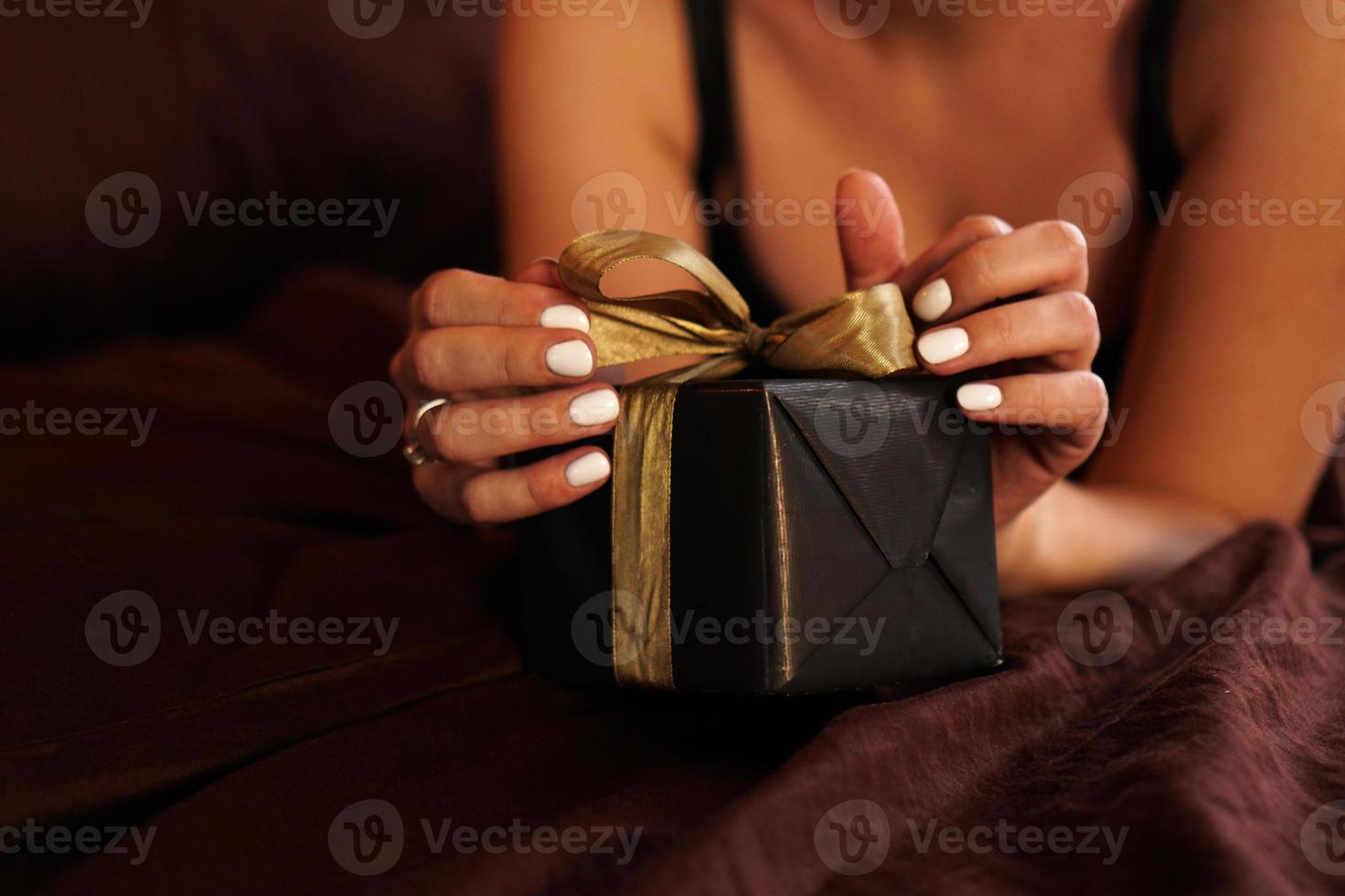 Die Frau öffnet ein Geschenk in einer schwarzen Schachtel mit einer goldenen Schleife foto