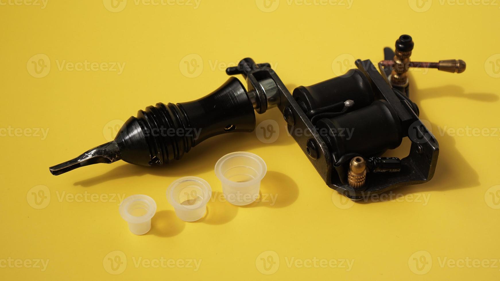 Tätowierausrüstung, Tätowierfarben-Kunststoffkappen und Tätowiermaschine auf Gelb foto