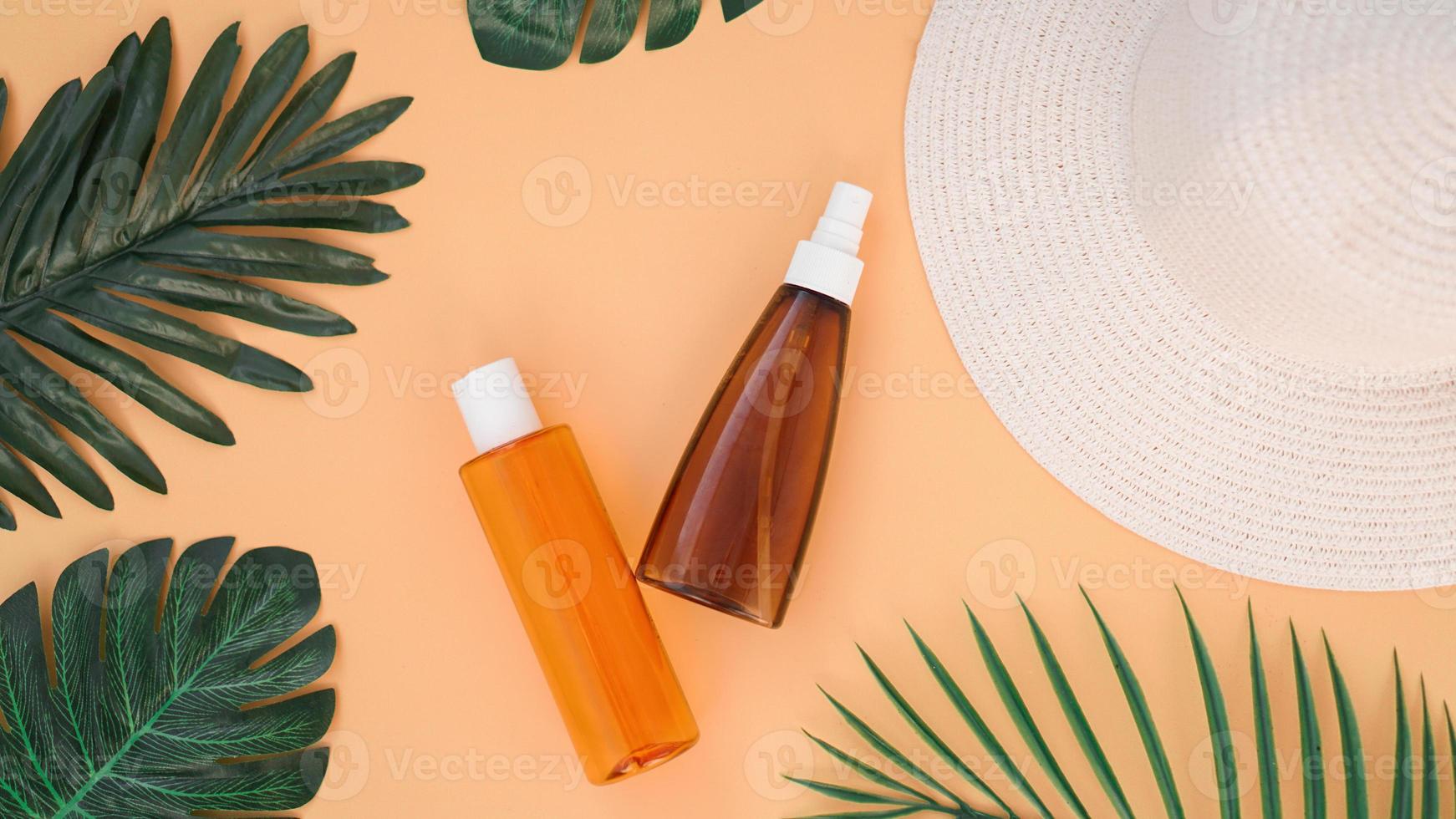 Sonnencreme, Sonnenhut, Lotionsflasche auf weichem orangefarbenem Hintergrund foto