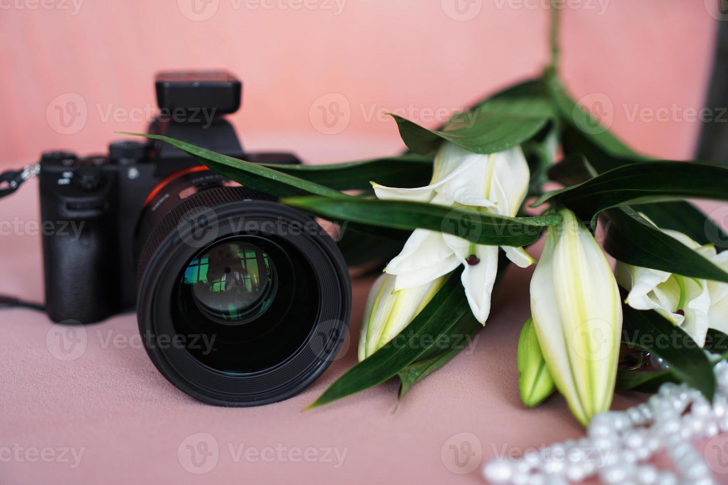 schwarze Kamera mit Objektiv und weißen Lilien und einer Perlenkette foto