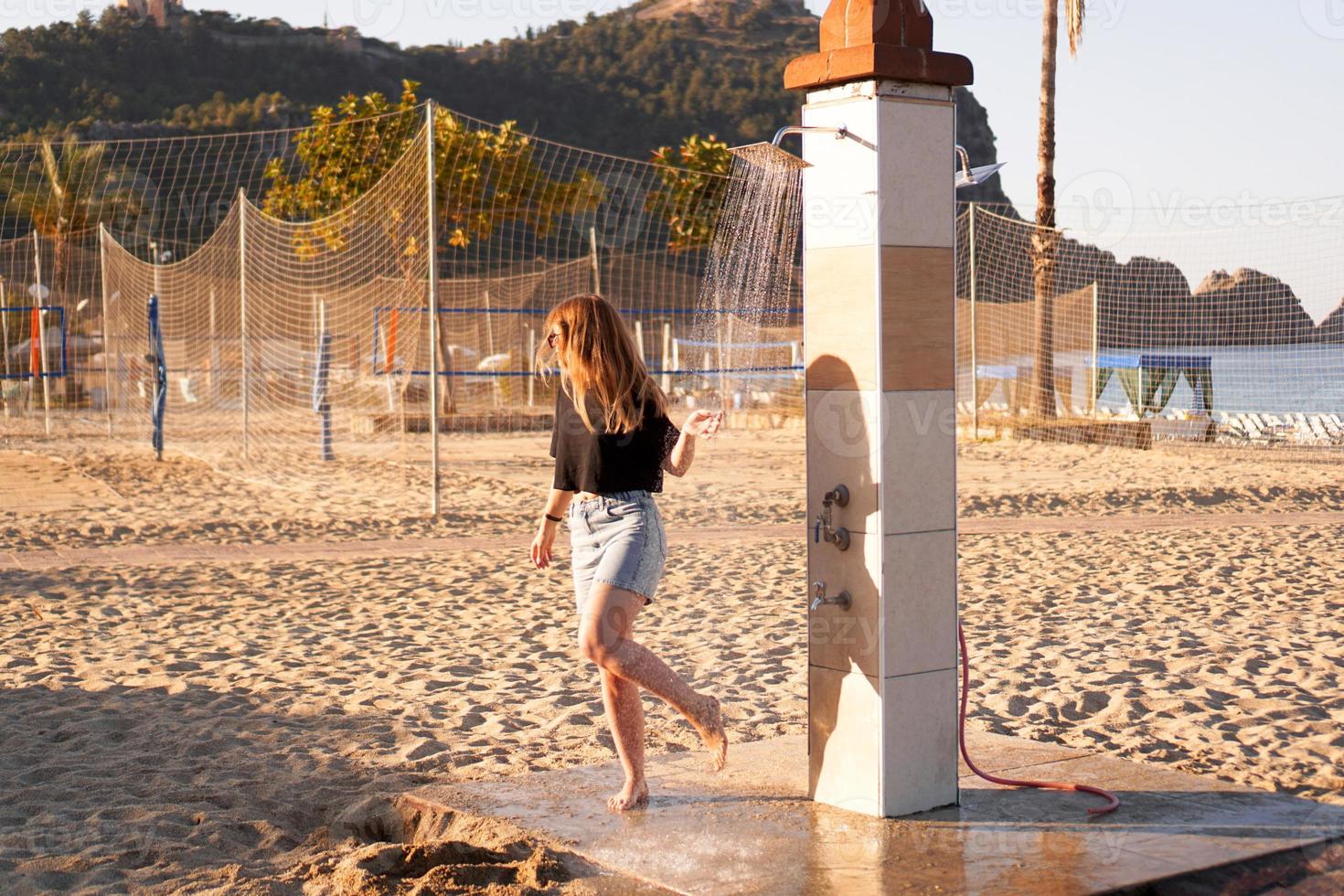ein Mädchen in kurzen Hosen und einem schwarzen T-Shirt am Strand in der Nähe der Dusche. foto