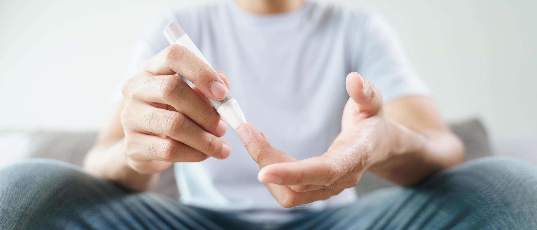 Mann verwendet Lanzette am Finger, um den Blutzuckerspiegel mit einem Glukosemeter zu überprüfen. foto