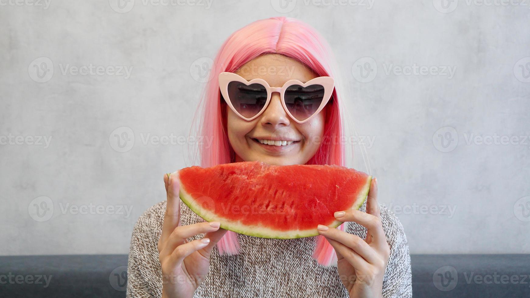 Frau mit Stück Wassermelone. Frau trägt rosa Perücke foto