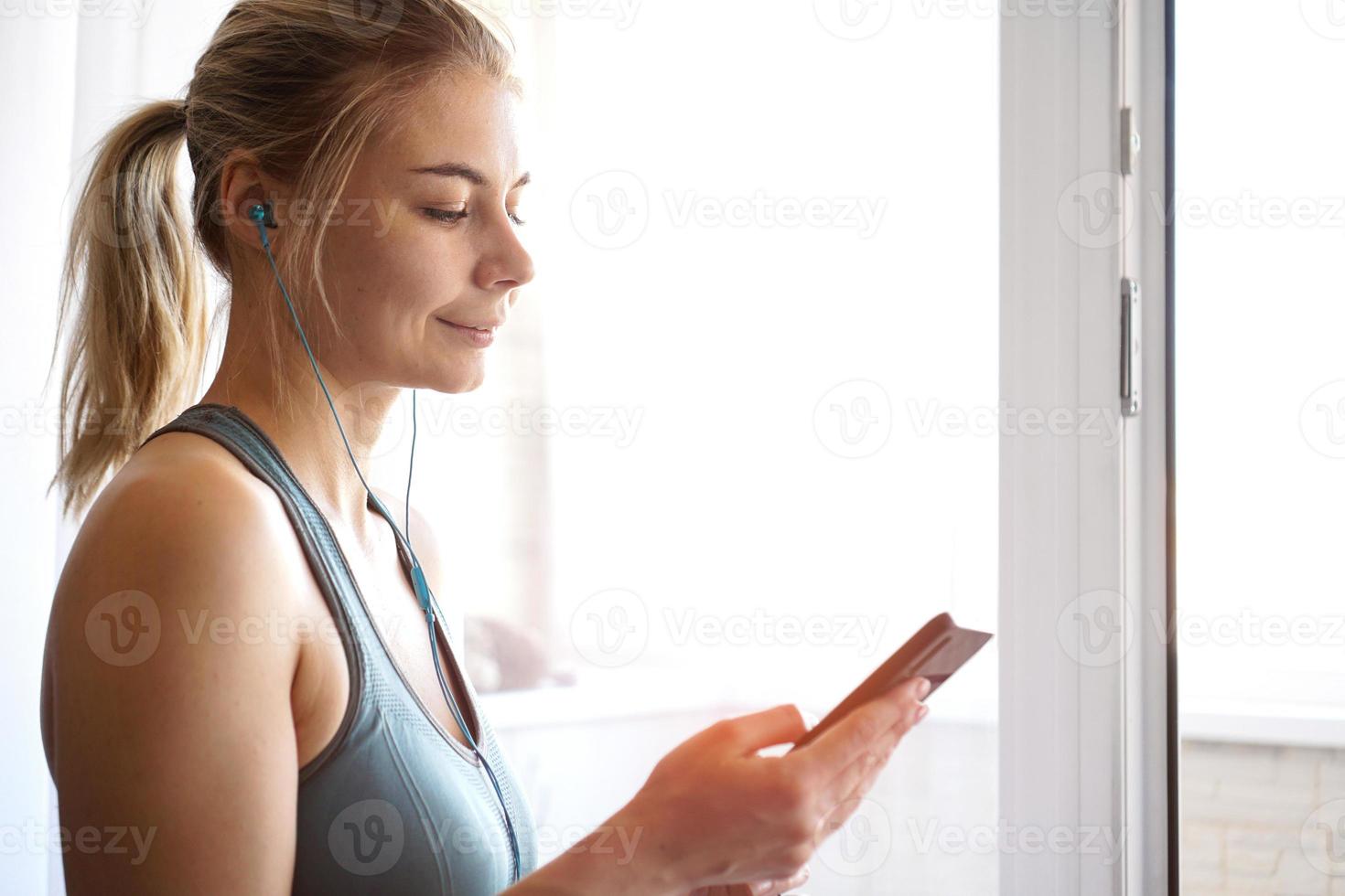 junges hübsches sportliches Mädchen steht in der Nähe des Fensters und hört Musik foto