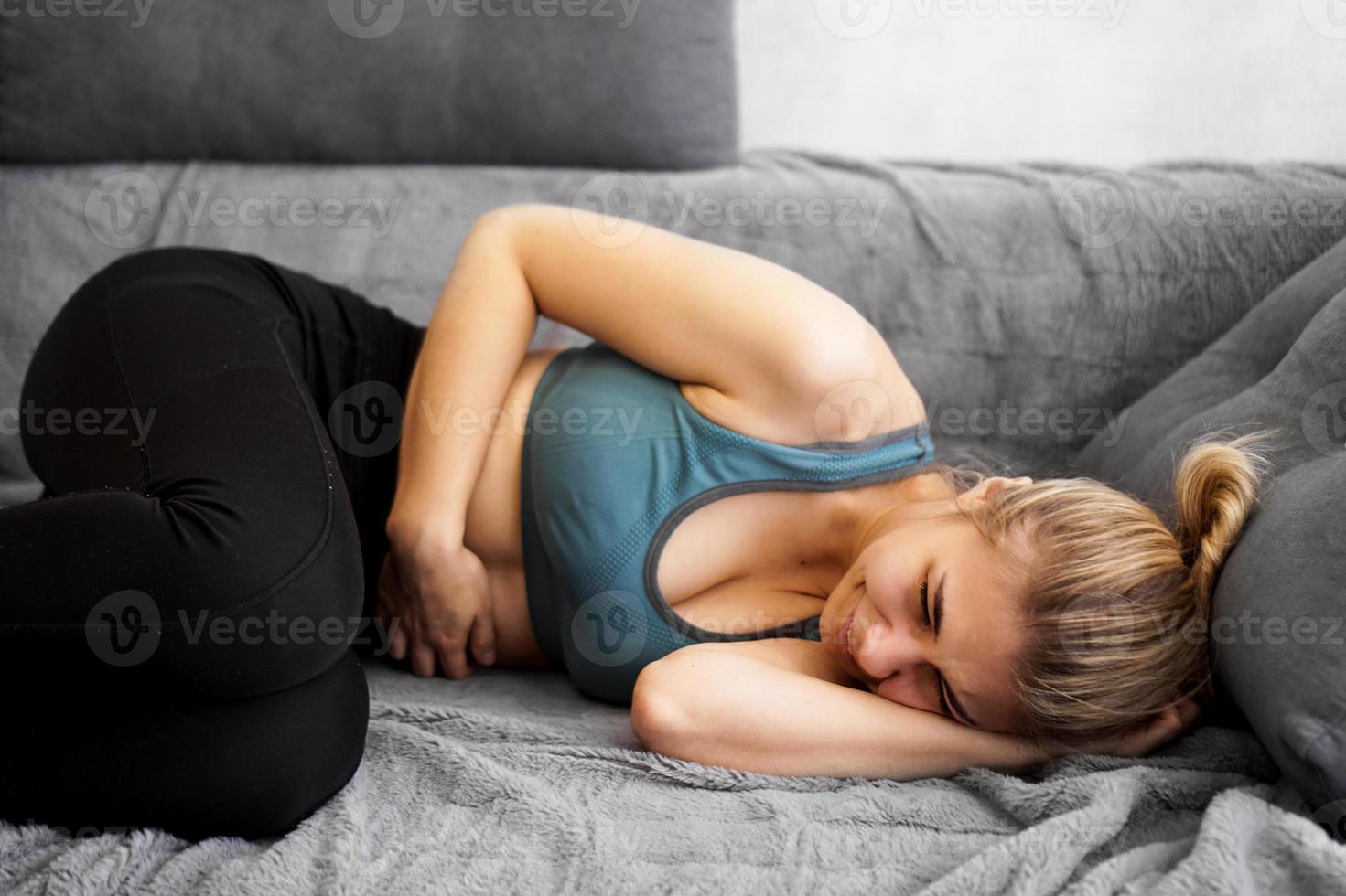 Seitenansicht einer Frau mit Bauchschmerzen, die zu Hause auf dem Sofa liegt foto