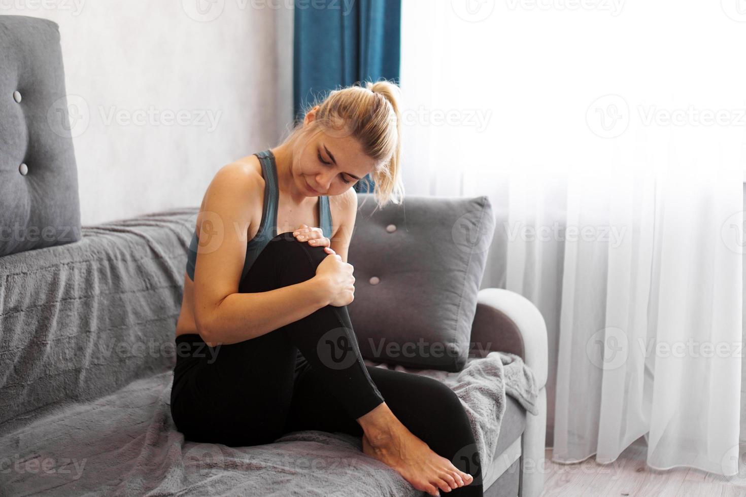 Frau hat Kniescheibenschmerzen, die auf dem Sofa sitzen und sich so krank fühlen foto