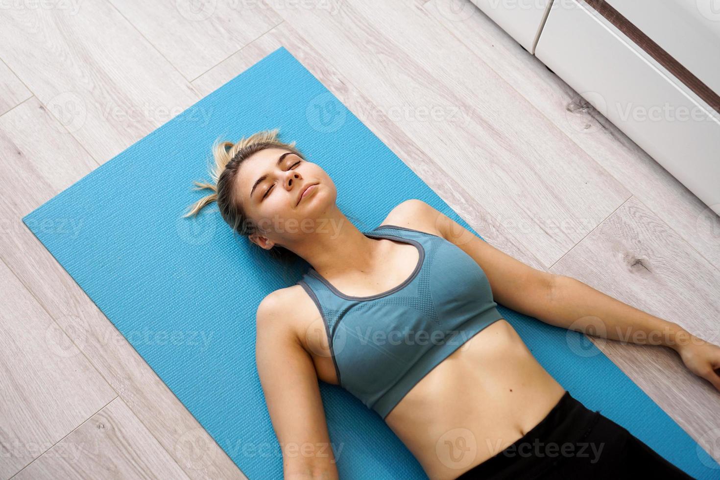 Blick von oben auf die schöne junge Frau, die nach dem Training auf der Yogamatte liegt foto