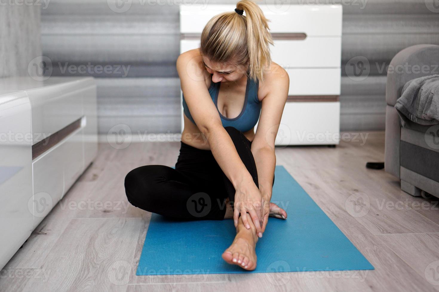 unglückliche Frau, die mit Knöchelverletzung auf der Yogamatte sitzt und Schmerzen verspürt foto