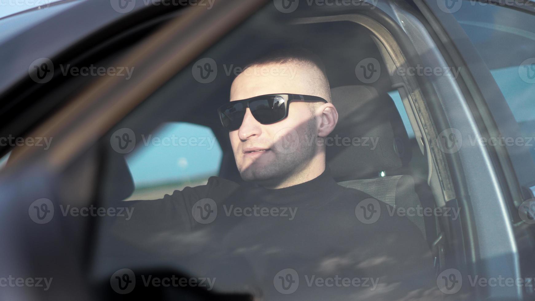 Seitenansicht eines selbstbewussten jungen, stilvollen Mannes mit Sonnenbrille in seinem Auto foto