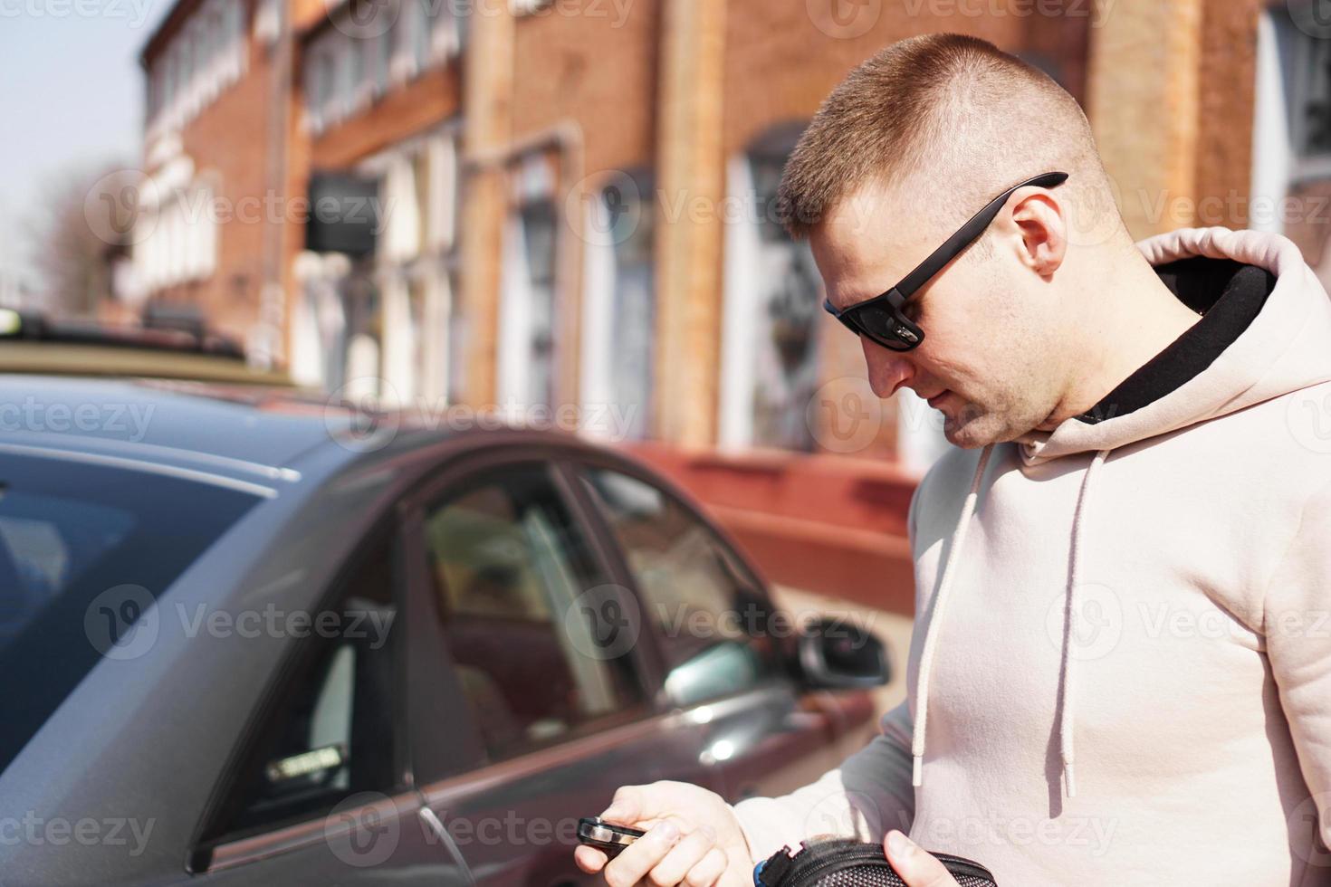 ein junger Mann neben seinem Auto an einem sonnigen Tag foto