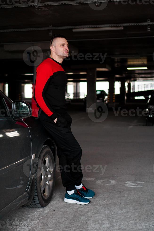ein junger Mann im Trainingsanzug steht neben einem Auto foto