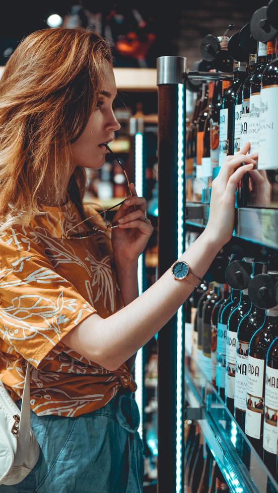 junge Frau wählt Wein im Supermarkt. foto