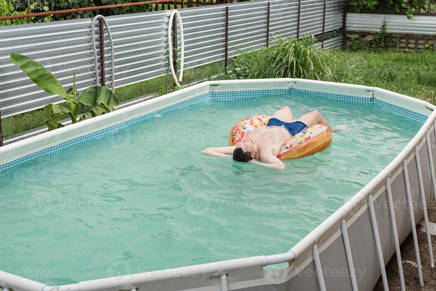 junger Mann beim Sonnenbaden auf aufblasbarem Schwimmschlauch im Pool foto