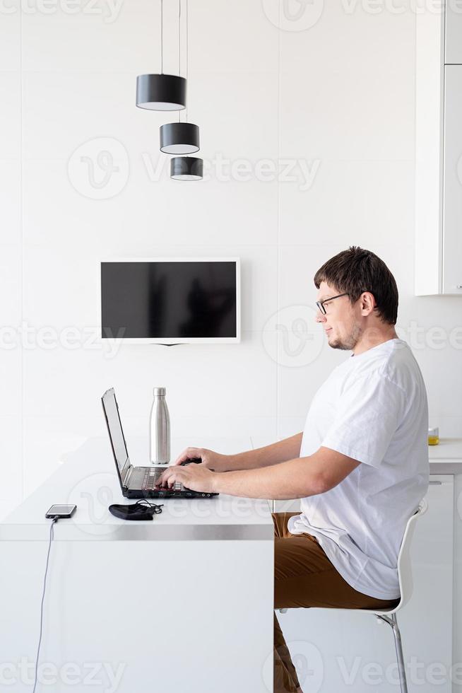 junger lächelnder Mann, der von zu Hause aus mit Laptop arbeitet foto