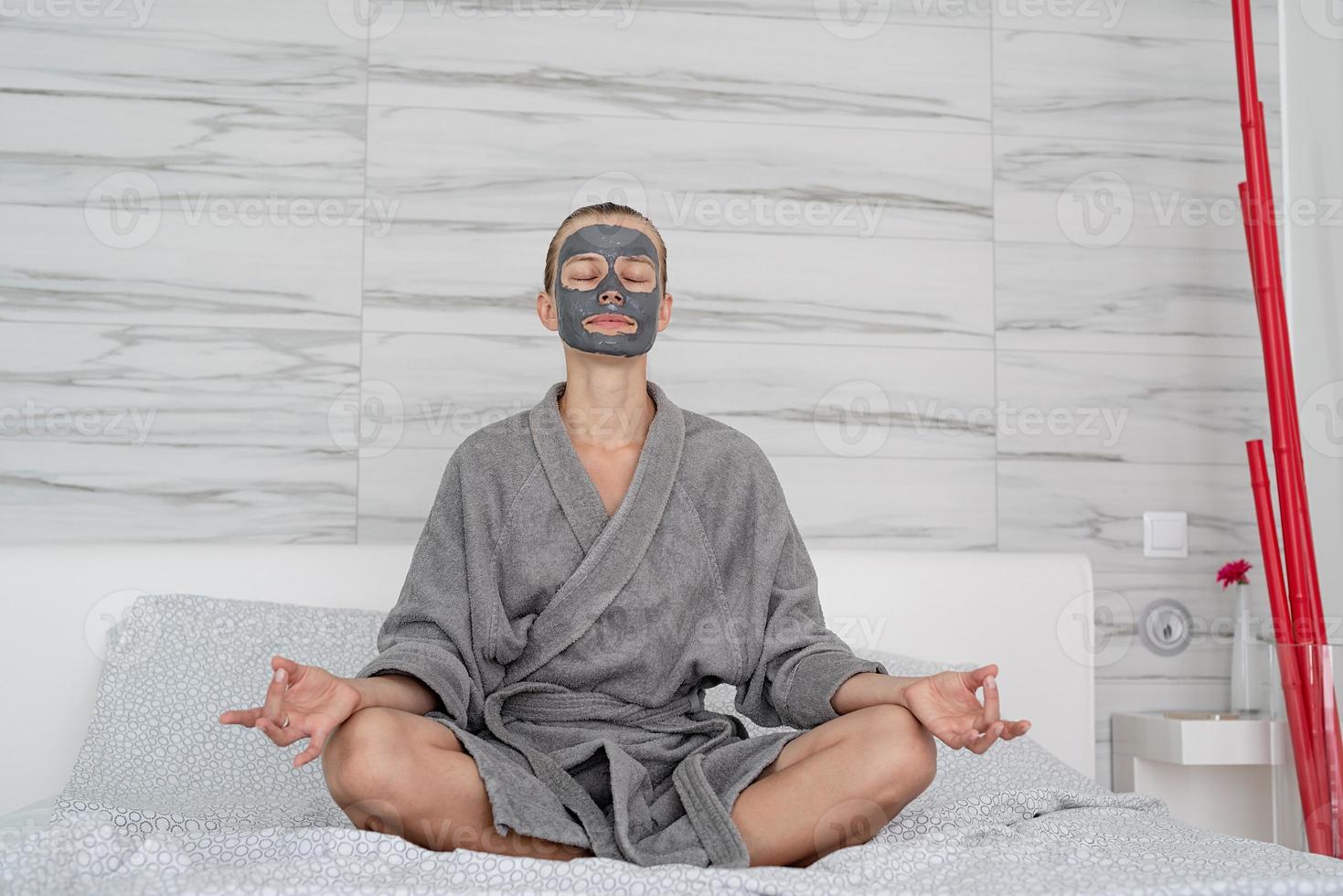 Frau mit Gesichtsmaske entspannt auf dem Bett sitzend foto