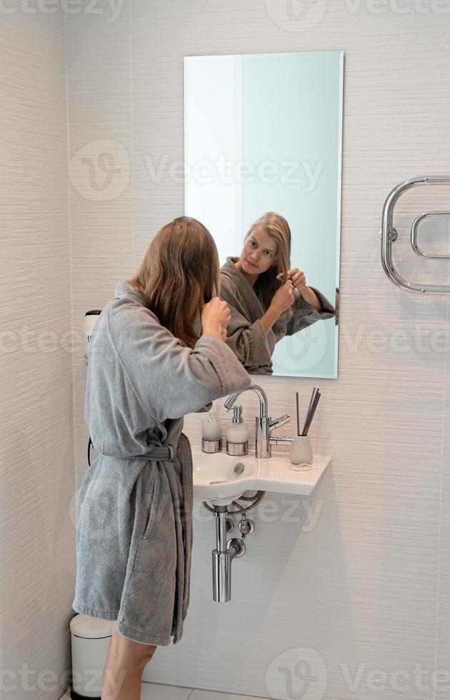 Frau bürstet sich die Haare und lächelt beim Blick in den Spiegel foto