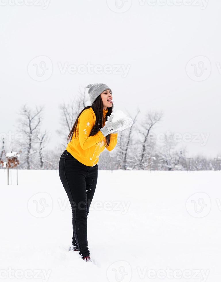 junge brünette Frau, die mit Schnee im Park spielt foto