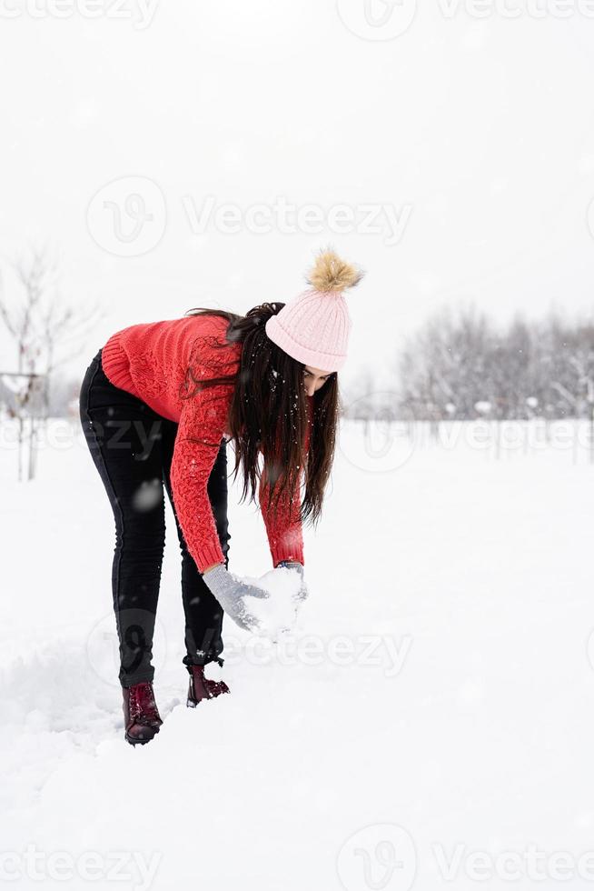 junge brünette Frau im roten Pullover spielt mit Schnee im Park foto