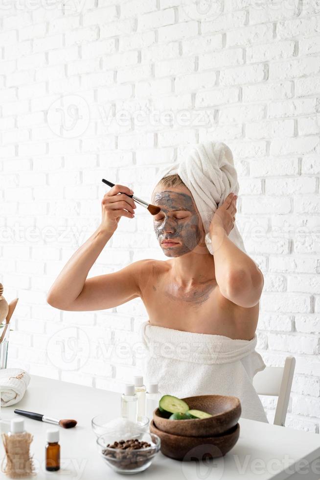 junge Frau, die mit einer Kosmetikbürste eine Spa-Gesichtsmaske auf ihr Gesicht aufträgt foto