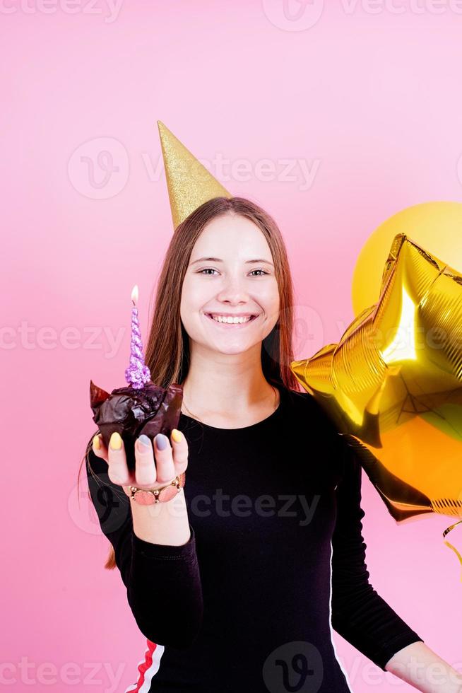 Teenager-Mädchen hält Muffin mit Kerzen und wünscht sich etwas foto