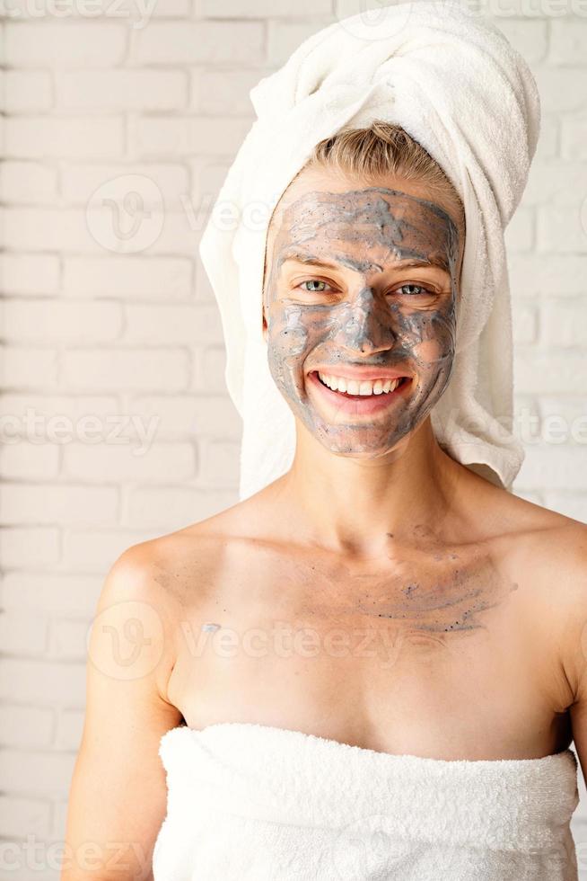 glücklich lächelnde Frau mit weißen Badetüchern mit Gesichtsmaske foto