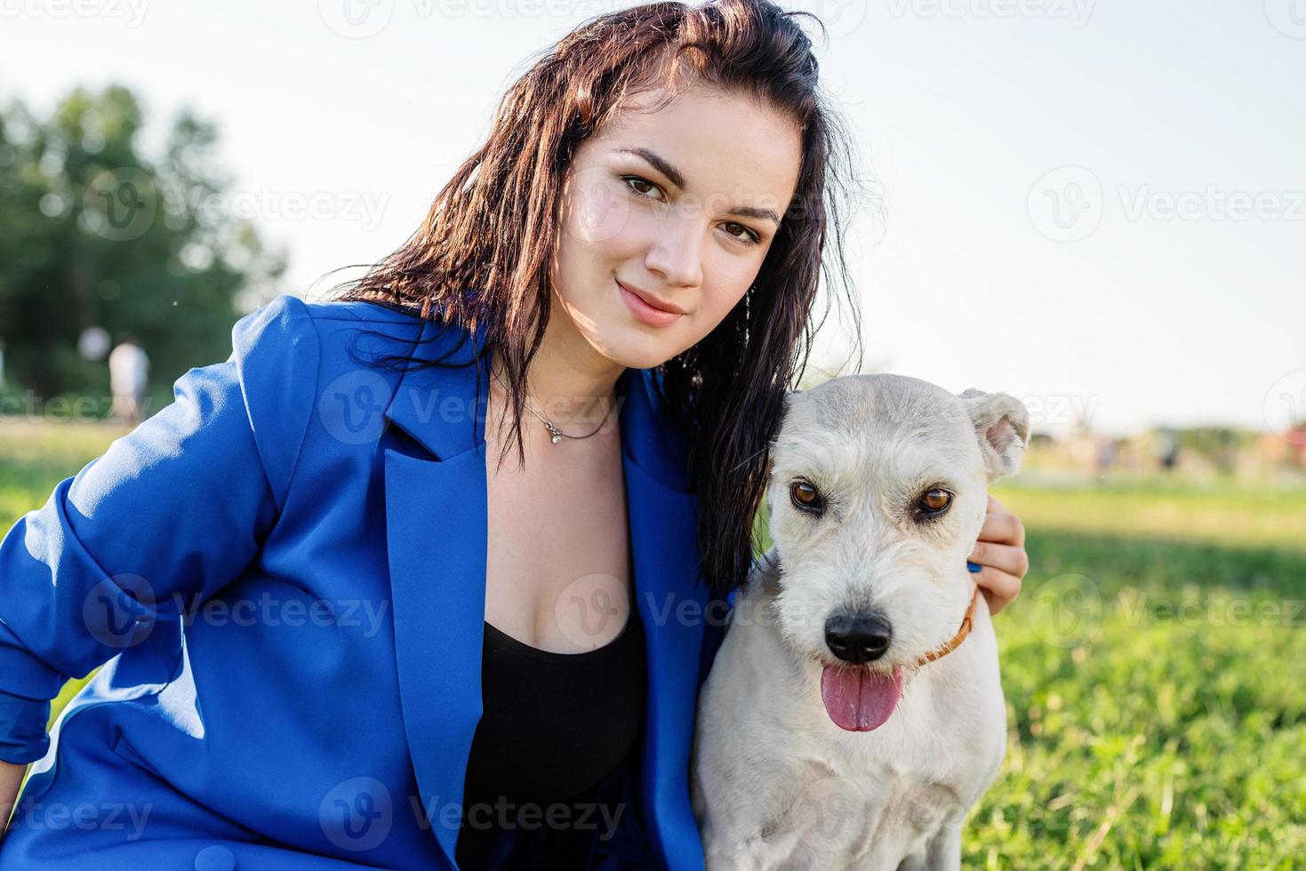 schöne junge frau, die im gras sitzt und ihren hund im park umarmt foto