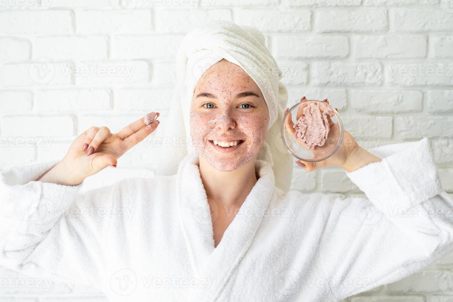 glückliche junge Frau, die Gesichtspeeling auf ihrem Gesicht anwendet foto