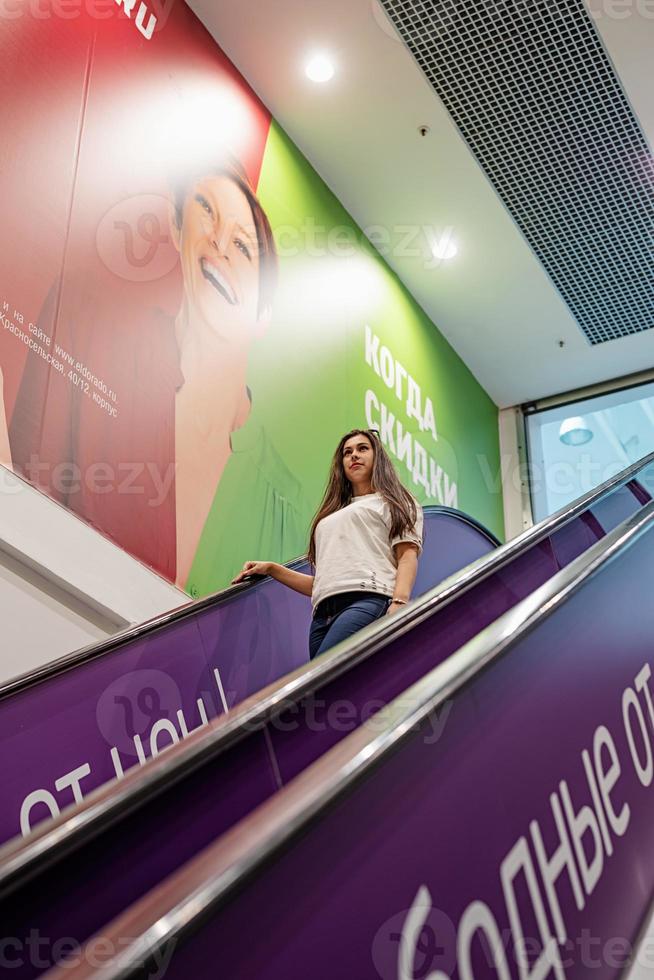 junge Frau steht auf Rolltreppe im Einkaufszentrum einkaufen foto