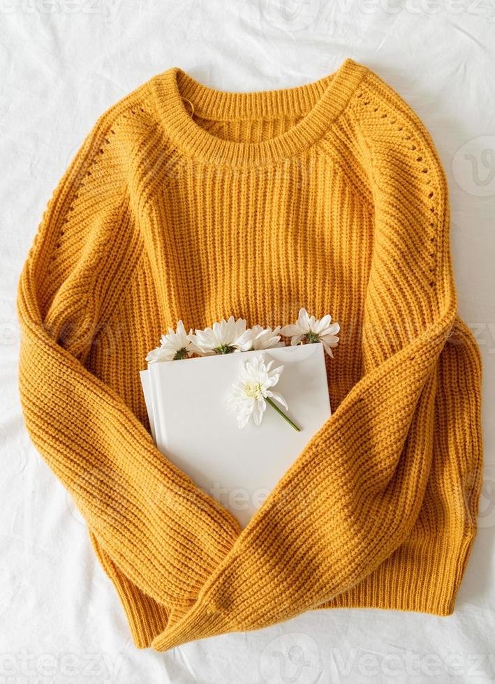 Draufsicht auf ein Buch mit weißen Chrysanthemenblüten auf gelbem Pullover foto