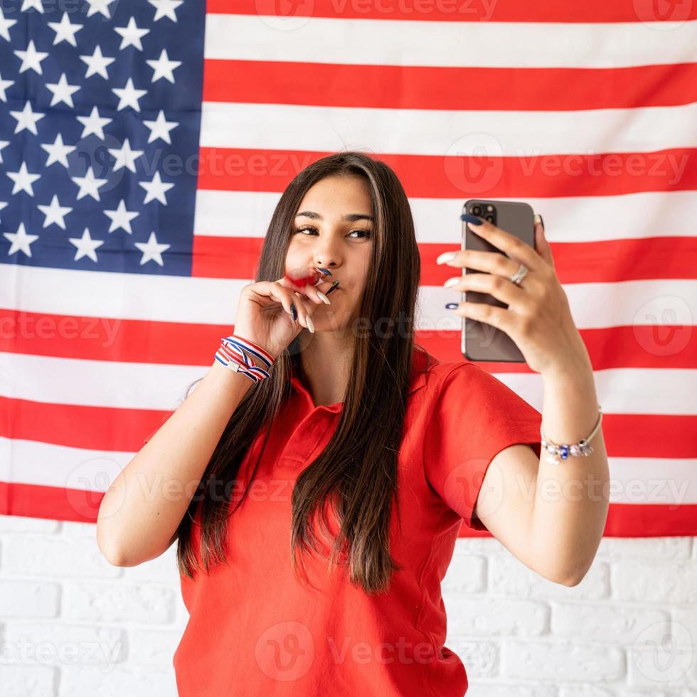 Frau mit einem Krachmacher, der ein Selfie auf dem Hintergrund der USA-Flagge macht foto