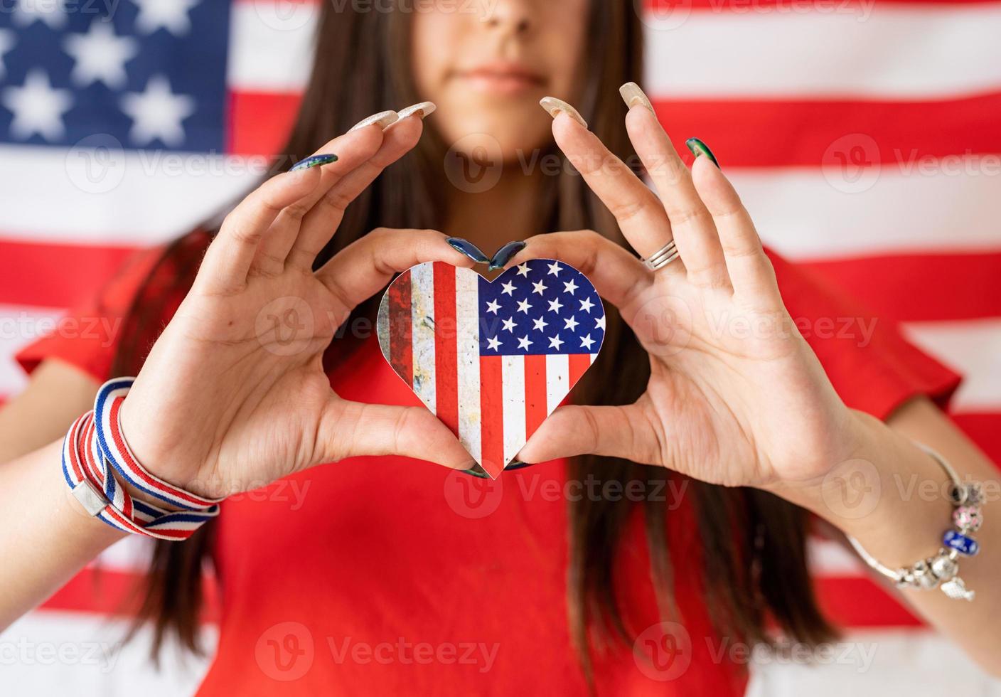 Frau, die eine kleine Nationalflagge auf dem Hintergrund der USA-Flagge hält foto