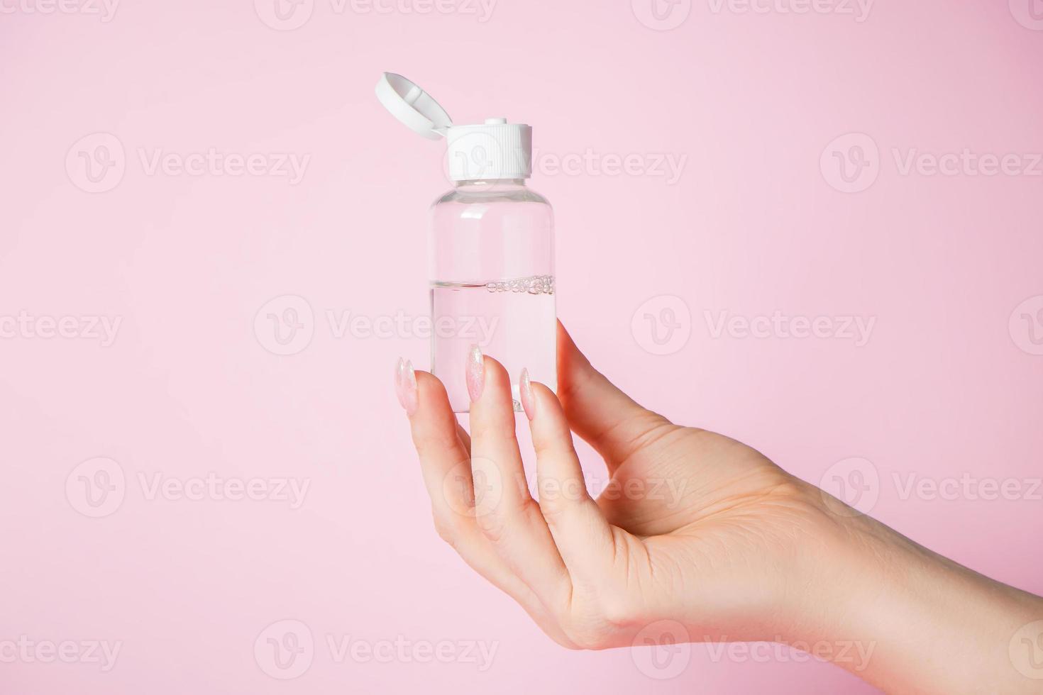 Hände mit einer Flasche auf rosa Hintergrund. Wellness- und Körperpflegekonzept. foto