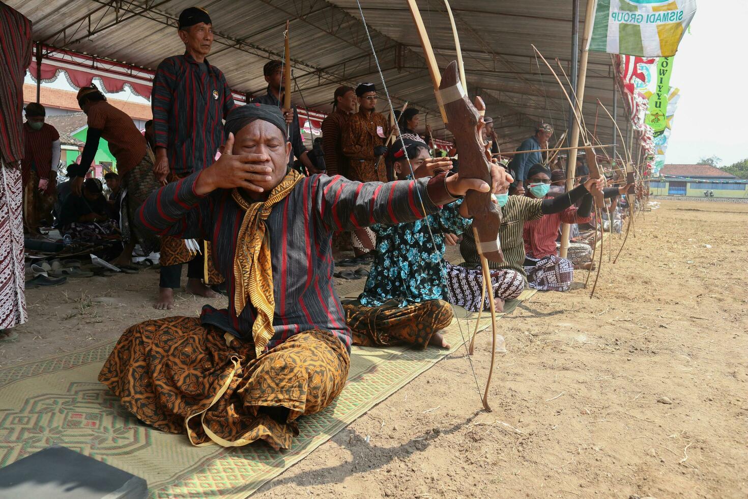 Klaten, Indonesien, August 15, 2023. männlich und weiblich Teilnehmer, gekleidet im javanisch Benutzerdefiniert gezogen seine Bogen durch Schielen zu leisten Konzentration von Ziel Richtigkeit im traditionell javanisch Pfeil trad. foto