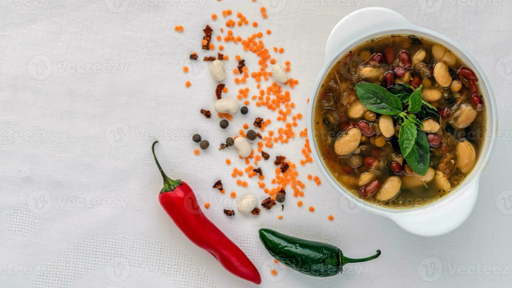Mexikaner Suppe von Sieben Arten von Bohnen, Nahaufnahme, auf ein Weiß Leinen- Hintergrund umgeben durch rot und Grün Pfeffer und Bohnen foto