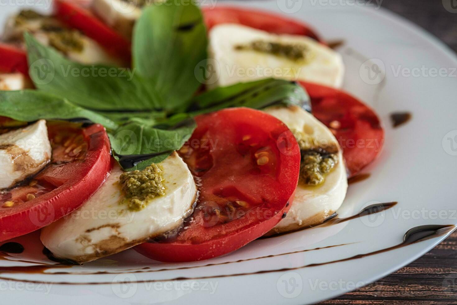 Weiß Teller von gesund klassisch köstlich Caprese Salat mit Tomaten und Mozzarella Käse mit Basilikum Blätter und Streifen von Soja Soße auf das Holz Hintergrund. schließen hoch. foto