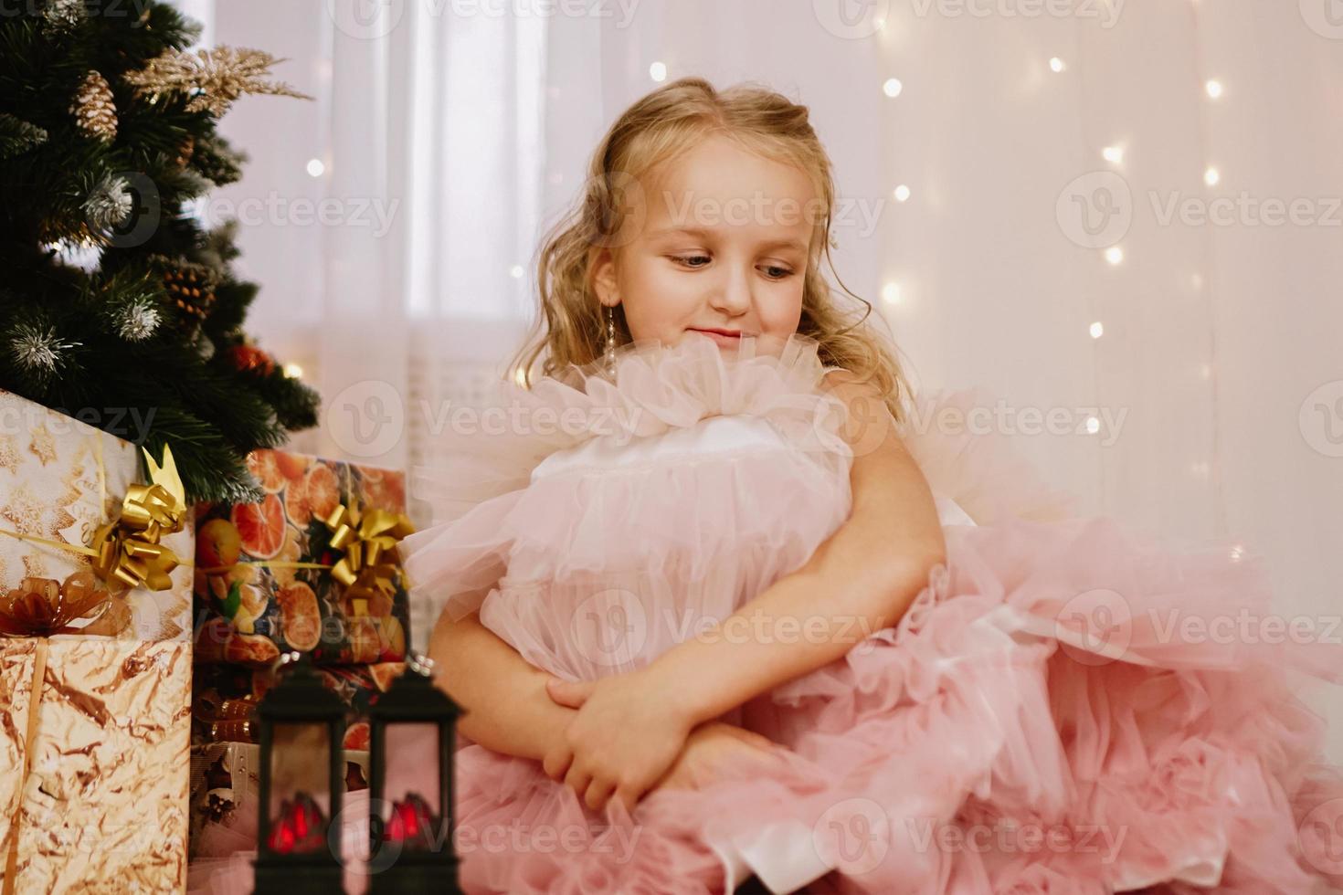 Mädchen in einem rosa Kleid neben dem Weihnachtsbaum foto