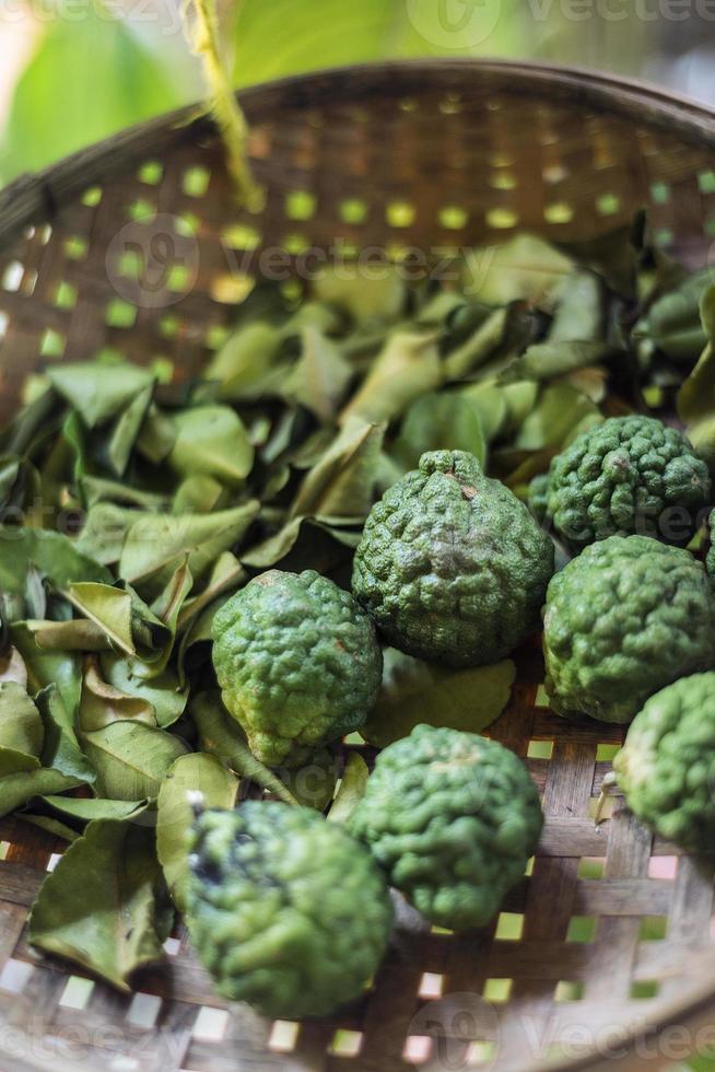 frische thailändische Kaffir-Limetten-Frucht und getrocknete Blätter im rustikalen Zutatenkorb foto