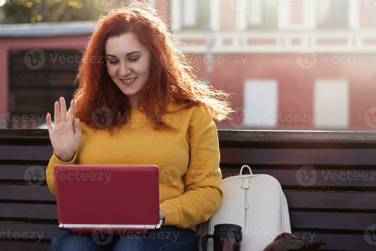 rothaarige frau im gelben pullover chattet per video. sie verwendet einen laptop, um im internet zu kommunizieren und zu arbeiten. foto