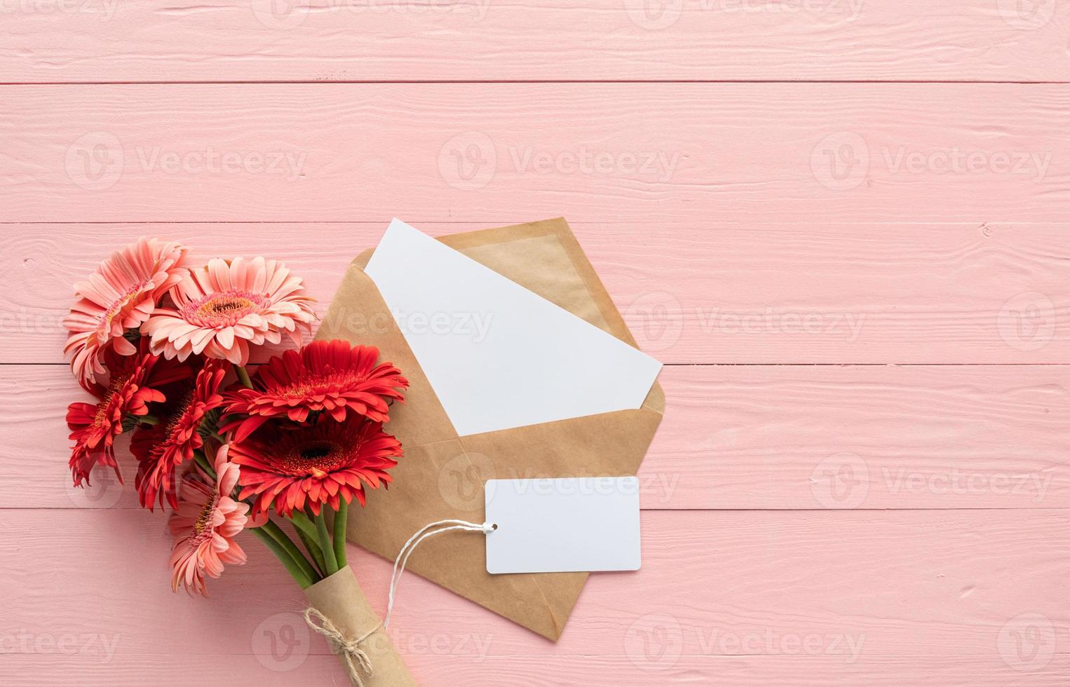 rote Gerbera-Gänseblümchen-Blumen, Umschlag und leeres Etikett auf rosa foto