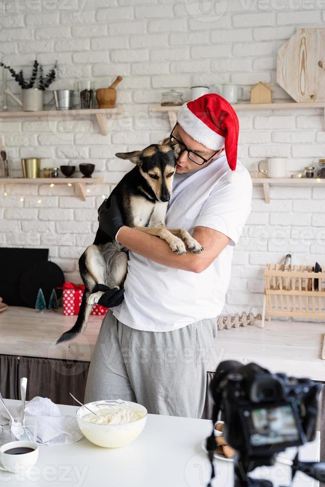 Koch in Weihnachtsmütze hält seinen Hund in den Armen beim Kochen in der Küche foto