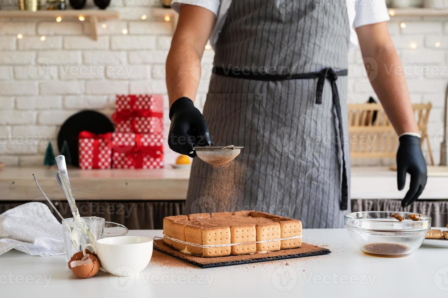 Koch kocht Dessert in der Küche und gießt Kakaopulver darauf foto