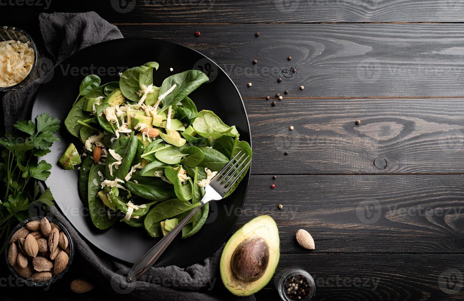 Draufsicht auf frischen Sommer-Avocado- und Spinat-Salat auf schwarzem Holz foto