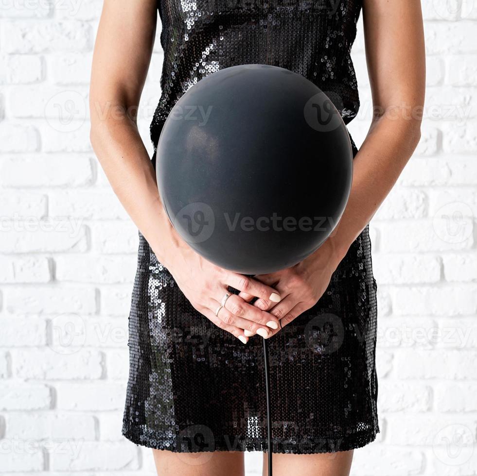 Frau im schwarzen Kleid, die einen schwarzen Ballon vors Gesicht hält foto