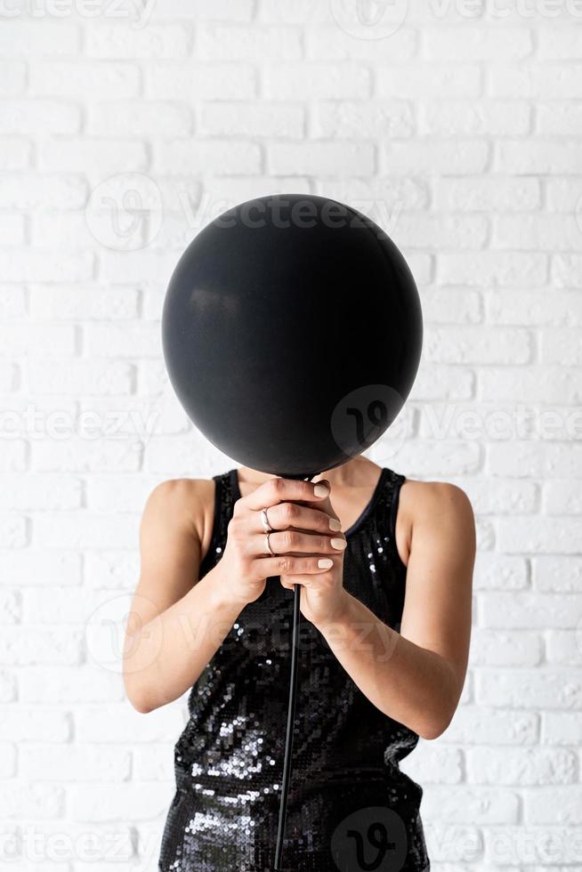 Frau im schwarzen Kleid, die einen schwarzen Ballon vors Gesicht hält foto