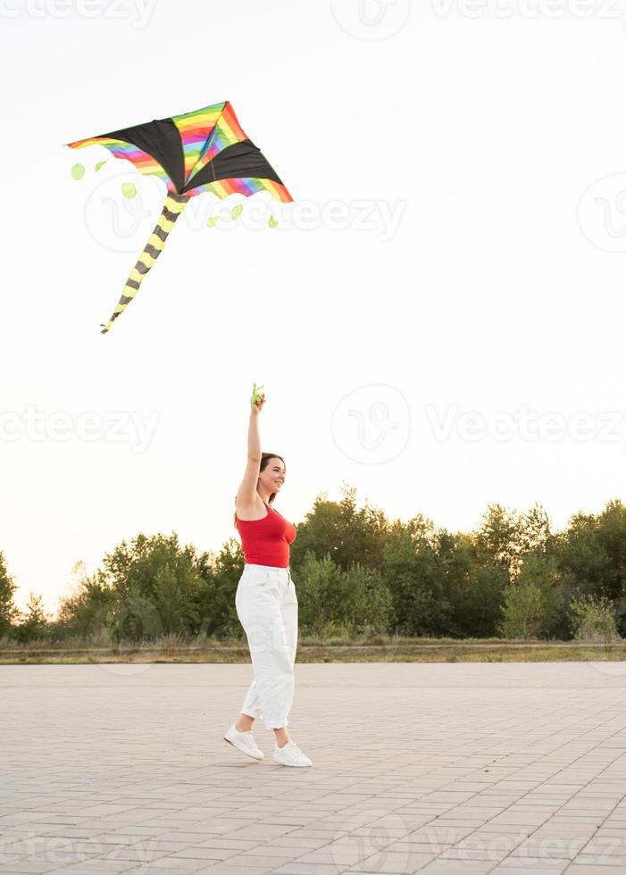 junge Frau, die bei Sonnenuntergang einen Drachen in einem öffentlichen Park fliegt foto