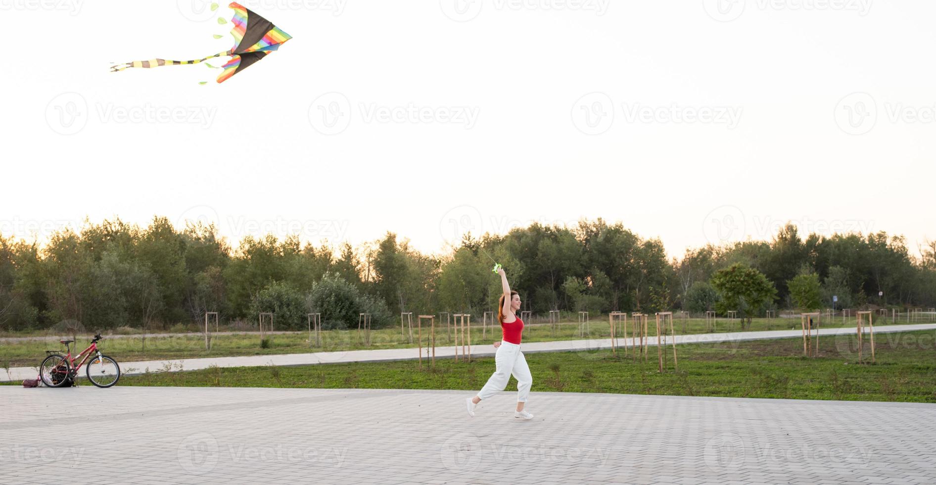 junge Frau, die bei Sonnenuntergang einen Drachen in einem öffentlichen Park fliegt foto