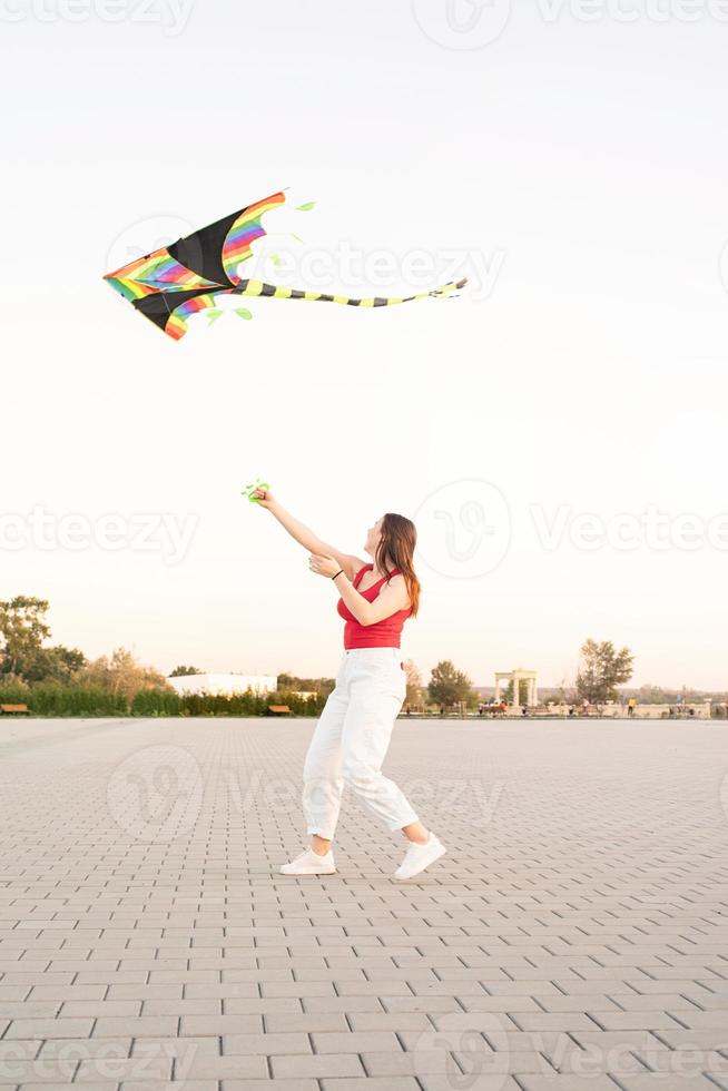 junge Frau, die bei Sonnenuntergang einen Drachen in einem öffentlichen Park fliegt foto